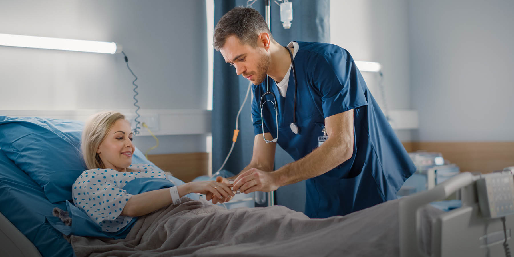 Ein Pflegefachmann steckt einer Patientin, die im Krankenbett liegt, ein medizinisches Gerät an den Finger.