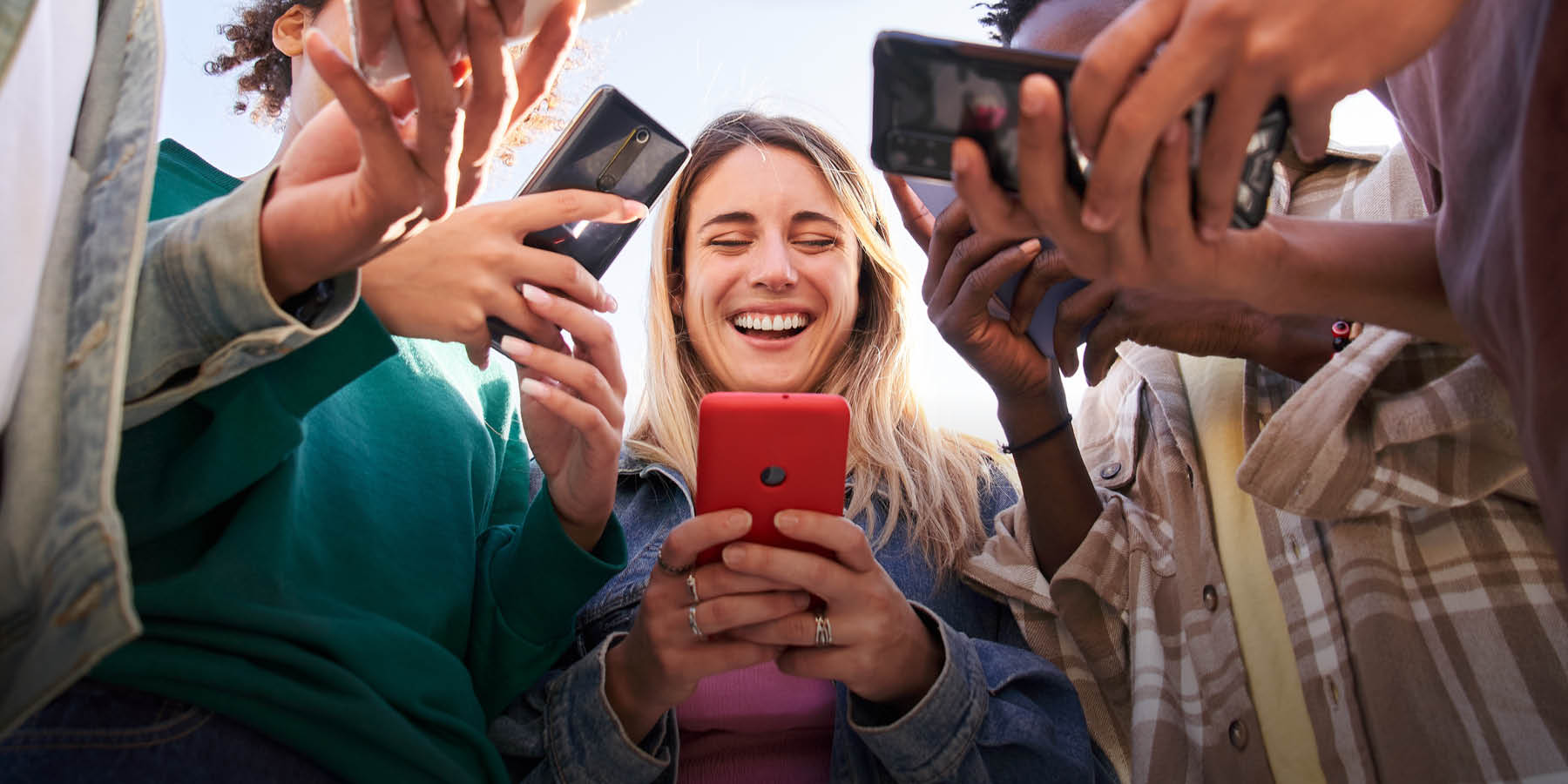 Das Bild in Froschperspektive zeigt eine Gruppe junger Menschen mit Handys in den Händen.
