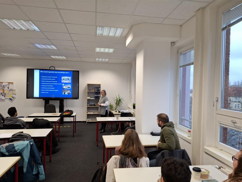 Auswärtiges Amt wirbt um angehende Fremdsprachenkorrespondent*innen In einem Klassenzimmer zeigt eine Vertreterin des Auswärtigen Amts an einem großen Bildschirm eine Präsentation. Die Schüler hören aufmerksam zu. Das Foto wurde aus der letzten Reihe aufgenommen, so dass man die Rückenansicht der Schüler*innen sieht.