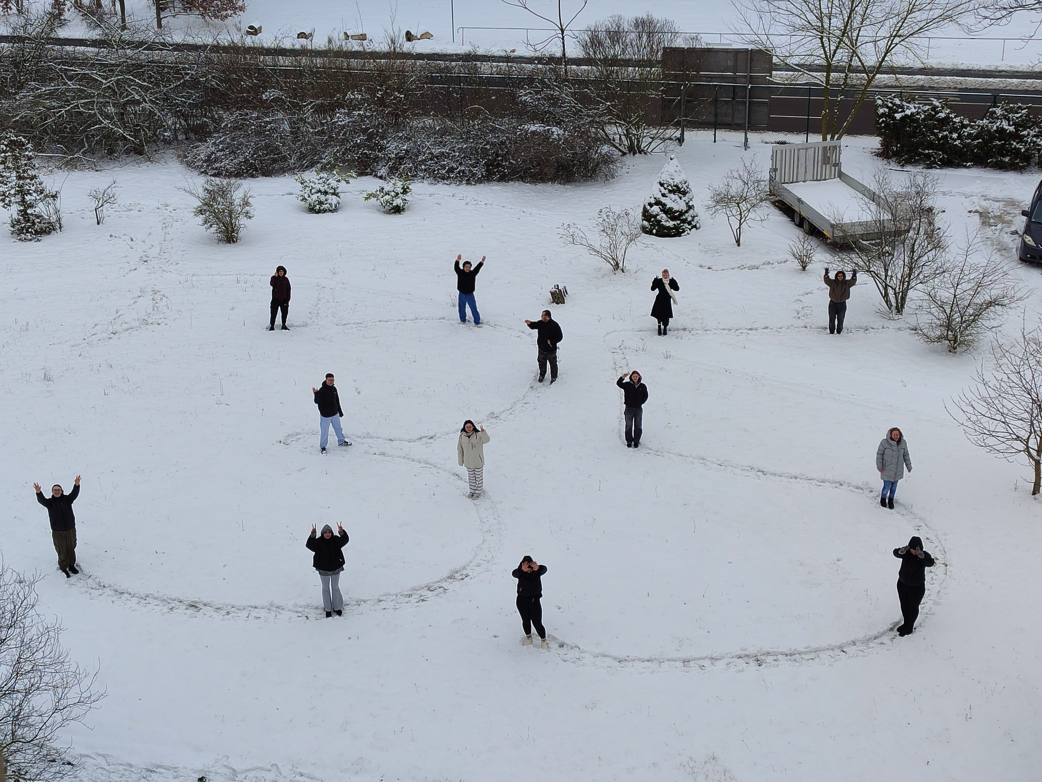 Sicht von oben auf einen schneebedeckten Platz, auf dem Schüler die Zahl 35 in den Schnee geschrieben haben; die Schüler stehen dabei und winken.