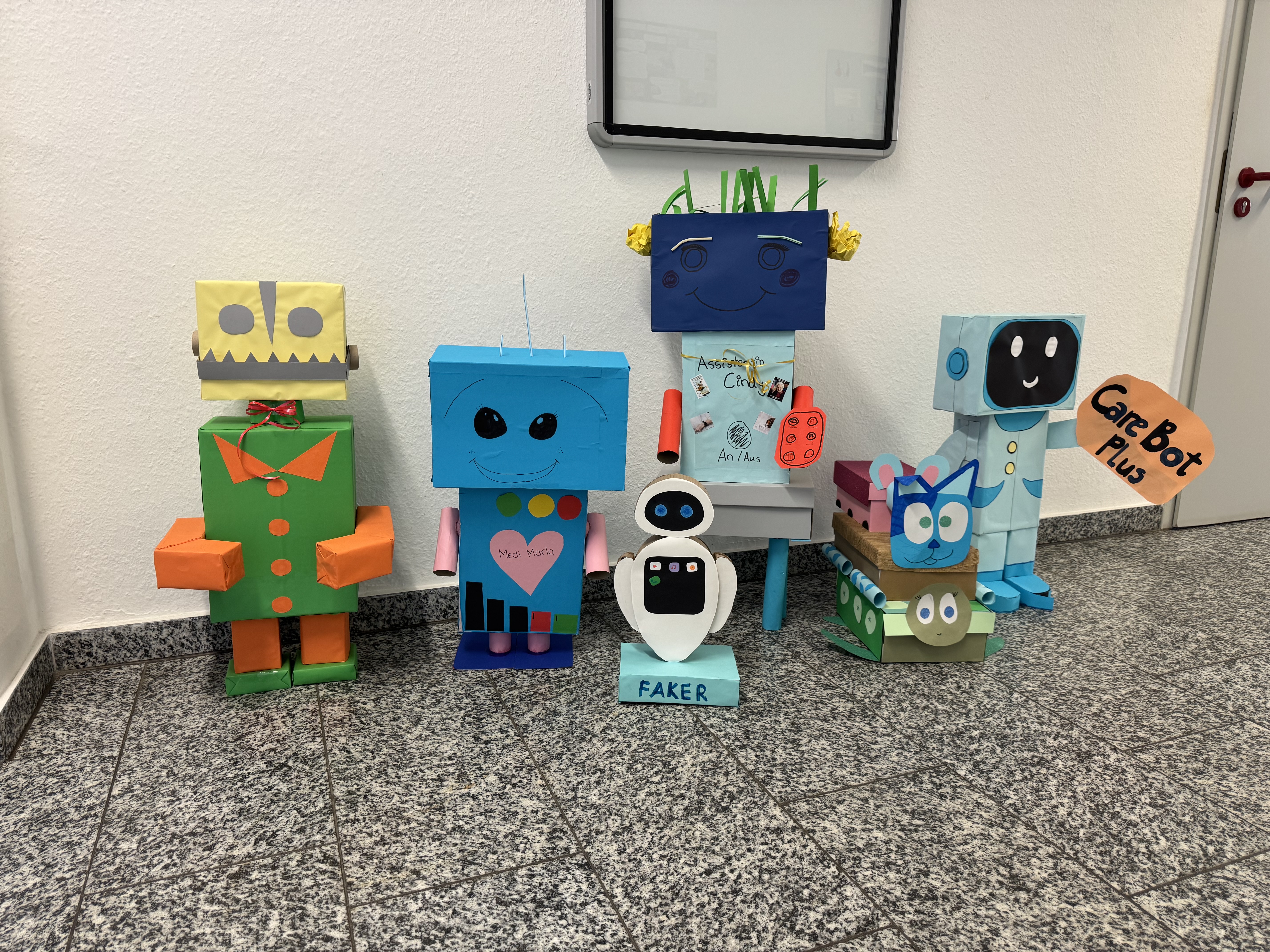 In einem Schulflur stehen sechs aus bunter Pappe gebastelte Roboter.