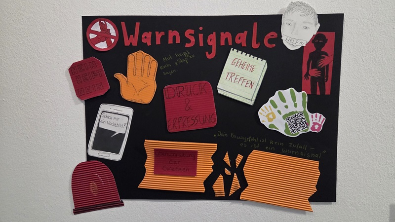 Eine Collage auf schwarzem Karton zeigt den Titel 'Warnsignale' in großen roten Buchstaben. Darunter sind verschiedene Elemente angeordnet: eine orangefarbene Handfläche, ein gezeichnetes Smartphone mit der Aufschrift 'Schick mir ein Nacktfoto!', eine grüne und orange Handabdruckgrafik, mehrere rote und orangefarbene Papierstreifen mit Texten wie 'Druck & Erpressung' und 'Geheime Treffen', sowie eine gezeichnete Figur mit rotem Gesichtsausdruck. Im Hintergrund sind handschriftliche Notizen und weitere kleine Zeichnungen zu erkennen. Die Gestaltung wirkt plakativ und nutzt starke Kontraste zwischen Schwarz, Rot und Orange.