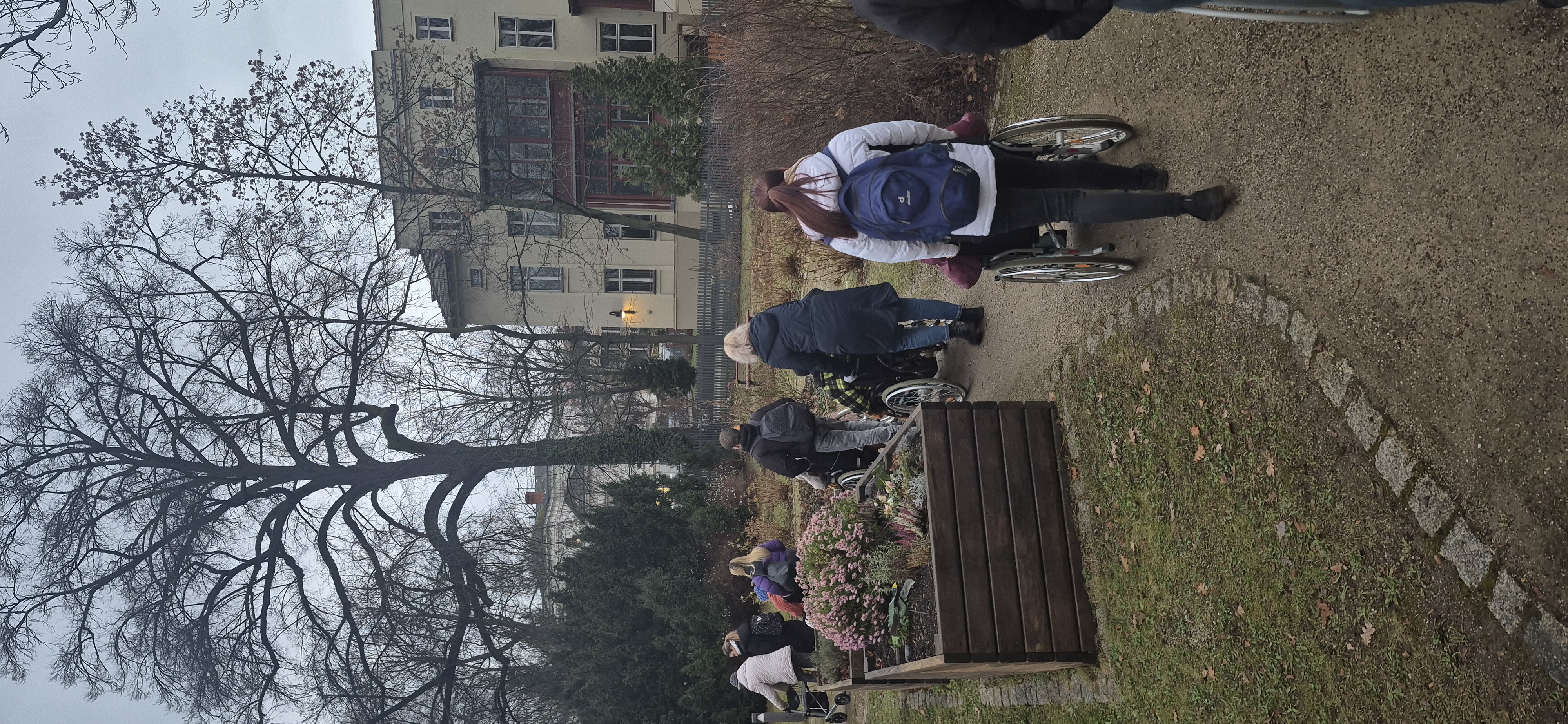 Schülerinnen und Schüler der Euro Akademie Görlitz begleiten Pflegeheimbewohnende im Rollstuhl auf einem winterlichen Parkweg beim gemeinsamen Ausflug zum Weihnachtsmarkt.