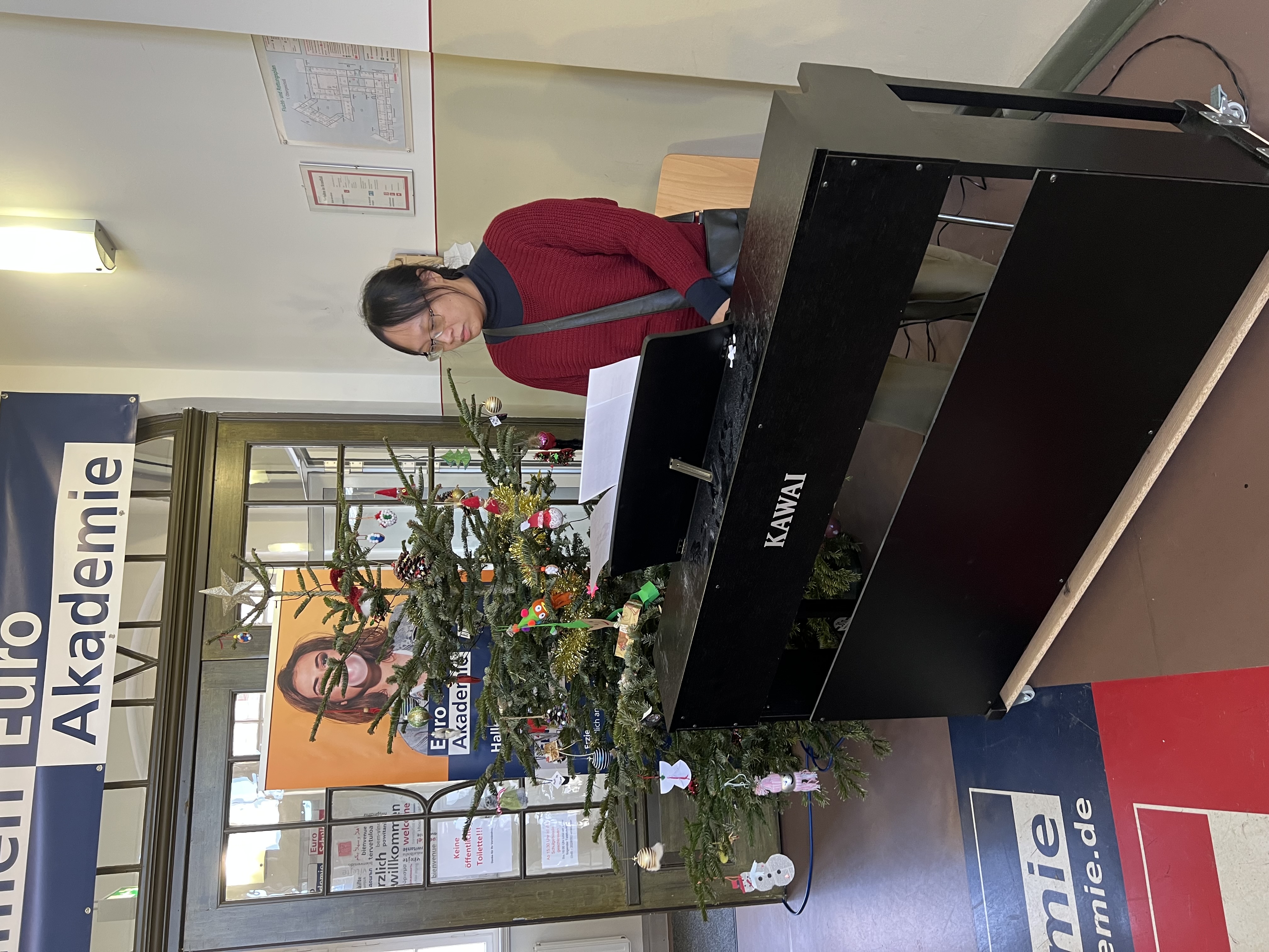 Im weihnachtlich geschmückten Eingangsbereich der Euro Akademie spielt eine Person an einem schwarzen E-Piano vor einem Weihnachtsbaum und einem Roll-up.