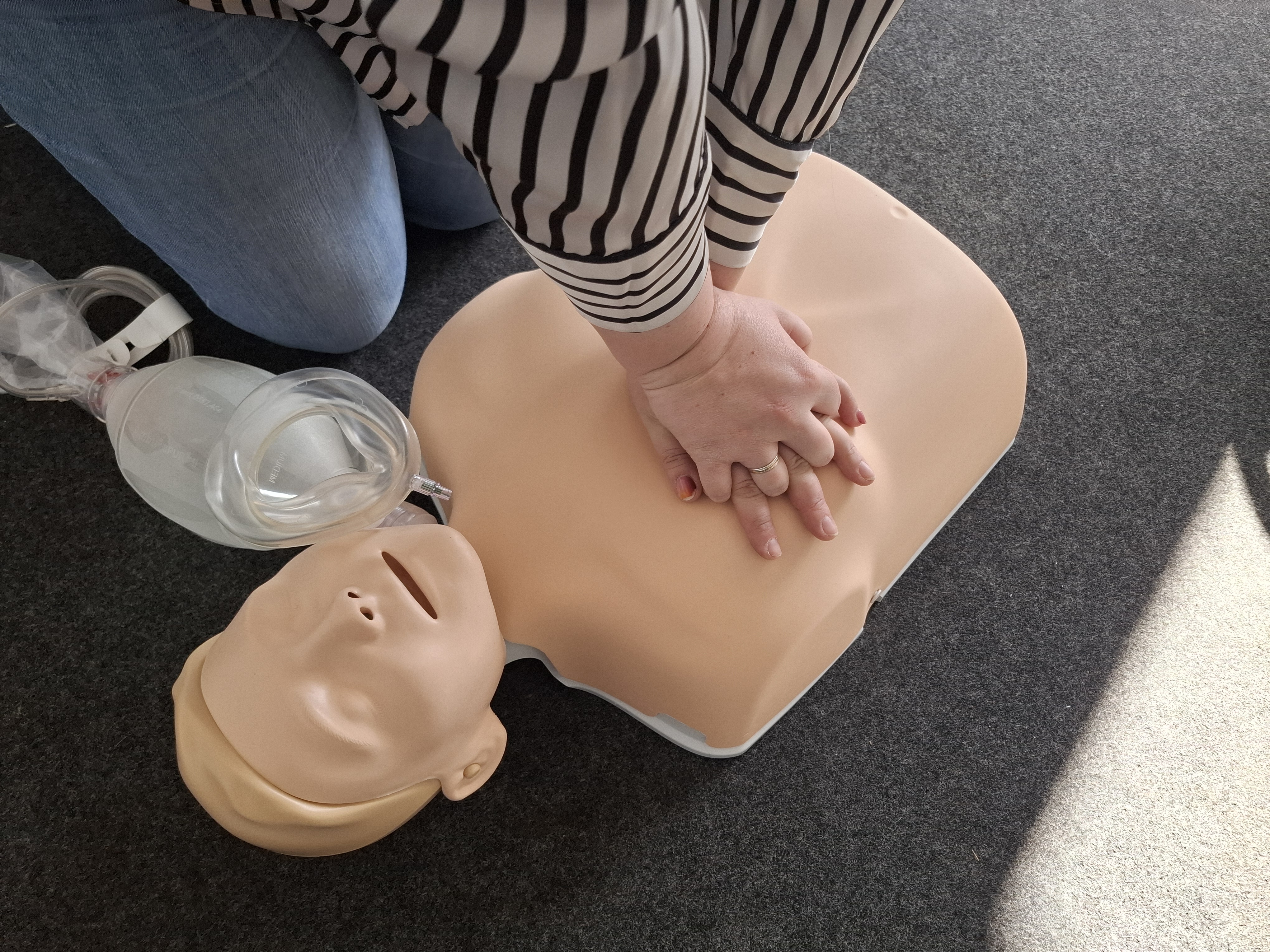 Nahaufnahme einer Herzdruckmassage an einer Reanimationspuppe mit Beatmungsbeutel während einer Erste-Hilfe-Schulung.