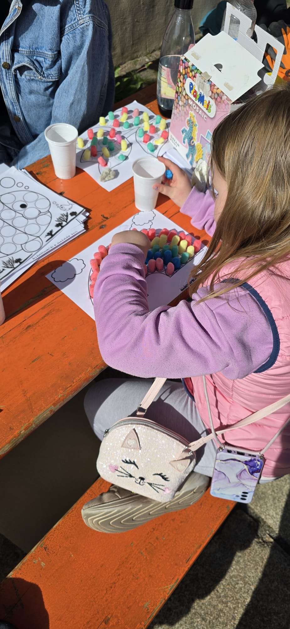 Ein Mädchen in einem lila Pulli bastelt ein Regenbogenbild.