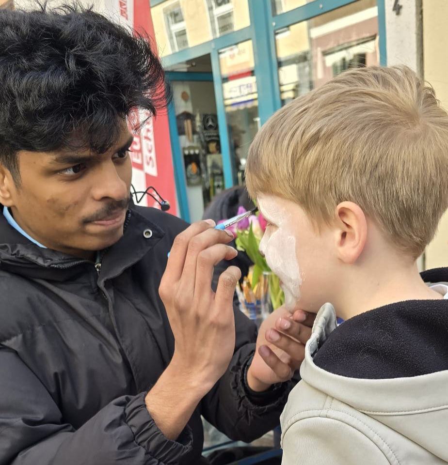 Ein junger Mann schminkt einem Jungen das Gesicht weiß.