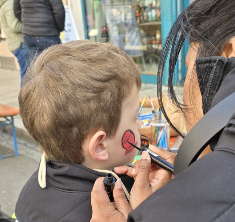 Eine Frau schminkt einem Jungen ein rotes Spiderman-Gesicht auf die Wange.