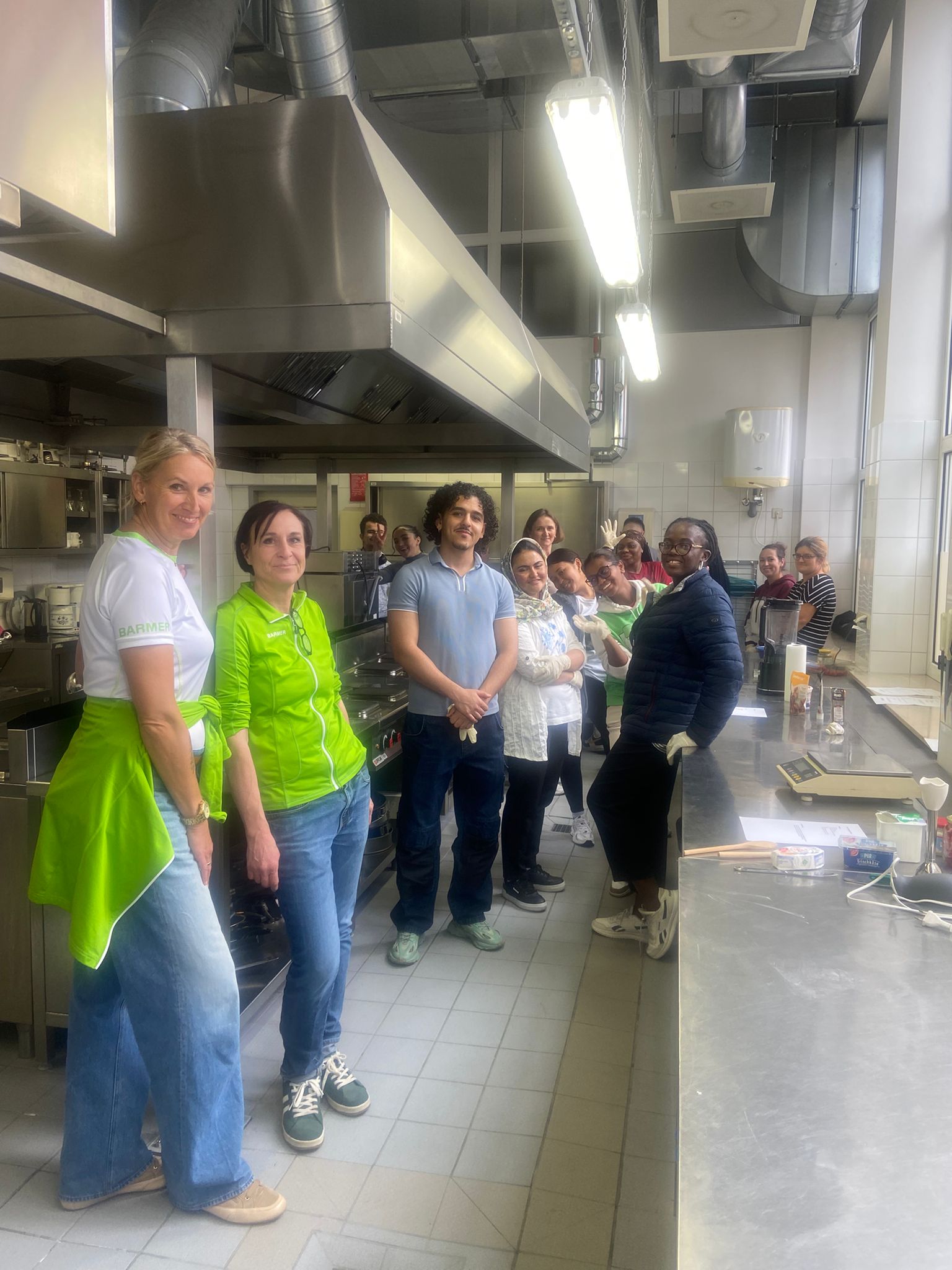 Gruppenfoto in einer Lehrküche: etwa ein Dutzend Teilnehmende stehen zwischen Edelstahl-Arbeitsplätzen und lächeln in die Kamera.