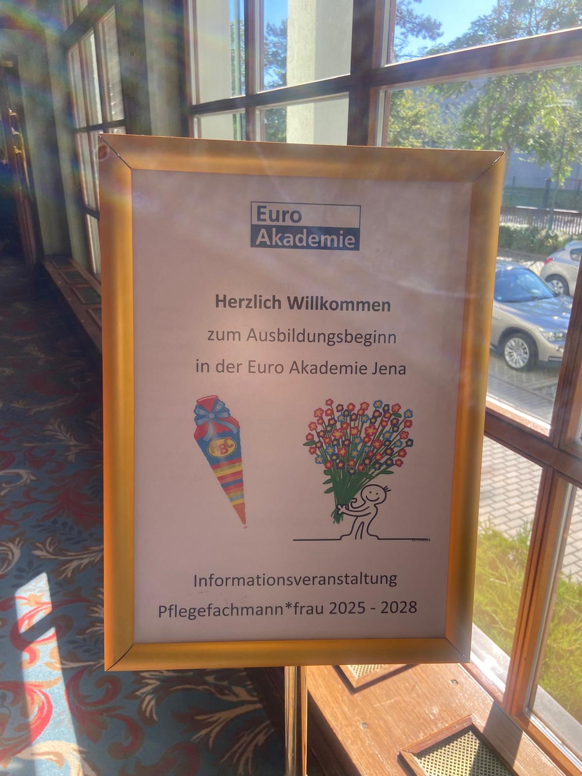 Willkommensschild im Foyer: „Euro Akademie – Herzlich Willkommen zum Ausbildungsbeginn … Informationsveranstaltung Pflegefachmann*frau 2025–2028“ mit Zuckertüte und Blumen-Illustration.