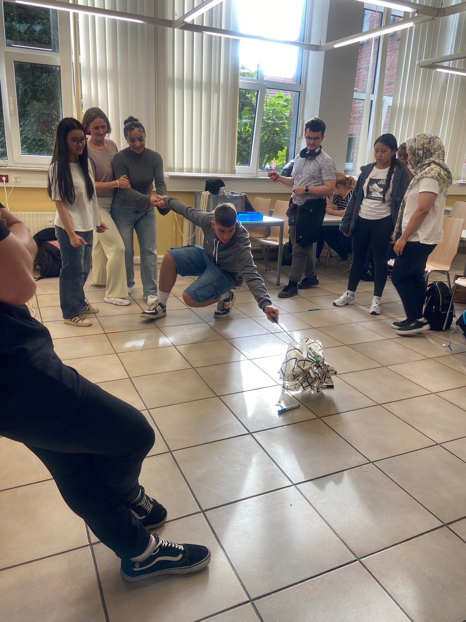 Weitere Teamübung: Gruppe hält sich fest, eine Person balanciert nach vorn und bewegt ein leichtes Gestell am Boden.