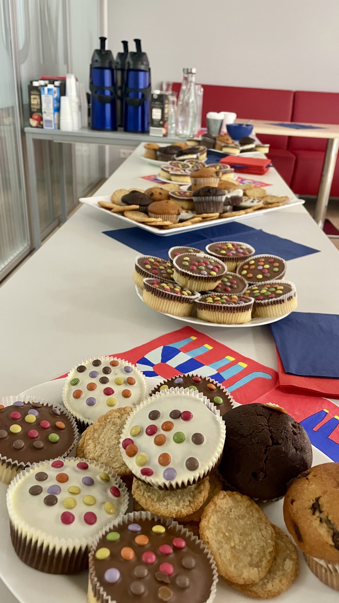 Buffet mit Muffins, Keksen und kleinen Kuchen, die mit Schokolade, Zuckerguss und bunten Schokolinsen verziert sind.