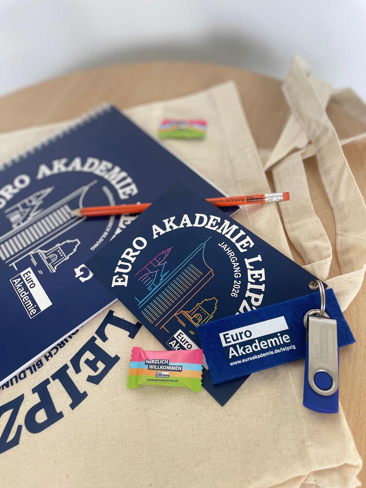 Begrüßungsmaterialien der Euro Akademie Leipzig mit Stoffbeutel, Notizblock, Postkarte, Bleistift, Schlüsselanhänger und Süßigkeit.