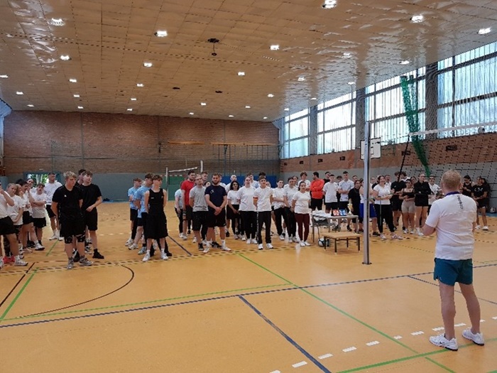 In Tradition: Ein gelungener Start ins neue Schuljahr – Kennenlernen von Schule und Gemeinschaft Die teilnehmenden Mannschaften stellen sich in der Turnhalle auf und hören dem Schiedsrichter zu, der am Volleyballnetz steht und zu ihnen spricht.