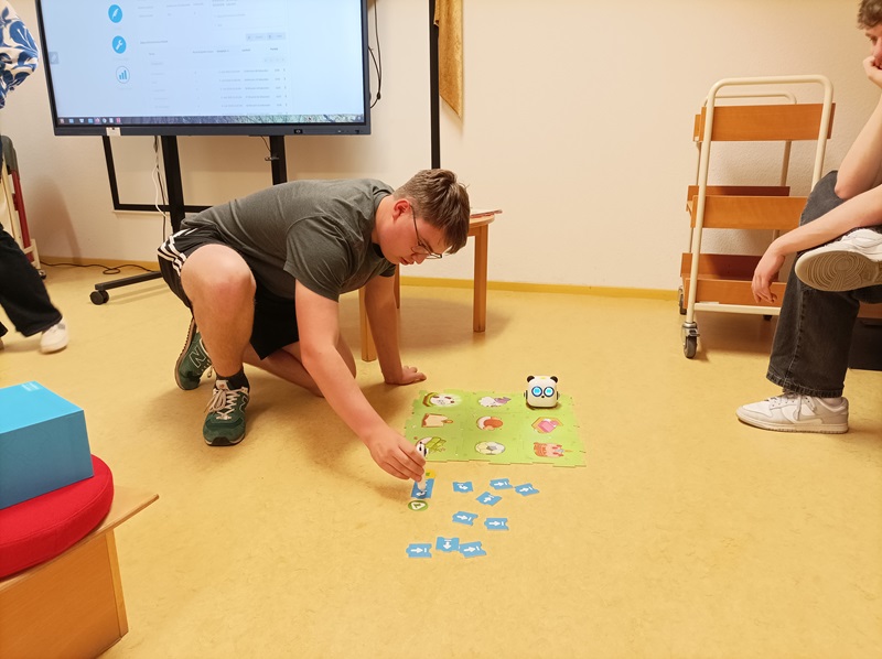 Sprache – ein Schlüssel zur Welt Ein Auszubildender der Euro Akademie Magdeburg sitzt vor einem Brettspiel für Kinder auf dem Boden der Bibliothek.