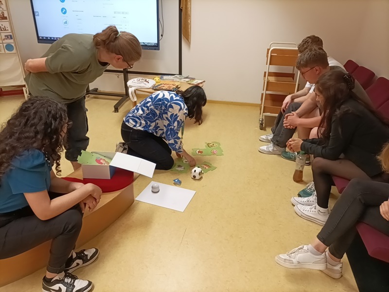 Sprache – ein Schlüssel zur Welt Die Auszubildenden der Euro Akademie Magdeburg sitzen im Kreis, einige auf dem Boden der Bibliothek, vor ihnen ein kleiner Fußball und Spielkarten.