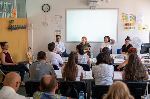 Sächsische Justizministerin zu Besuch an der Euro Akademie Meißen In einem Klassenzimmer sitzen drei Frauen und ein Mann direkt vor der Tafel und richten den Blick auf eine Frau, die an der Seite auf einem Stuhl Platz genommen hat. Diese spricht offenbar, während die vier Personen vor der Tafel ebenso zuhören wie die Schülerinnen und Schüler, von denen man nur die Rückenansicht sehen kann.