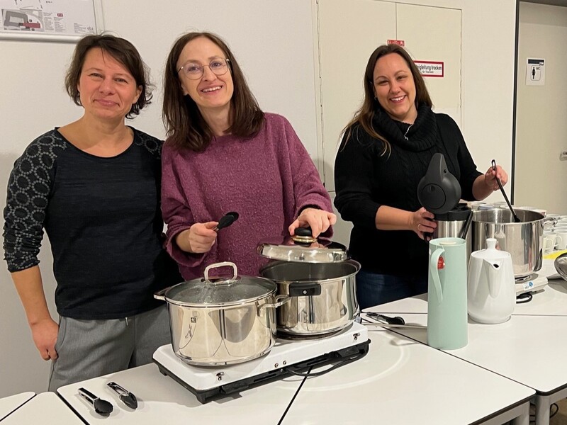 Drei Frauen stehen hinter den Tischen, auf denen die Kochtöpfe auf Warmhalteplatten thronen: Links die Würstchen, rechts der Kinderpunsch.