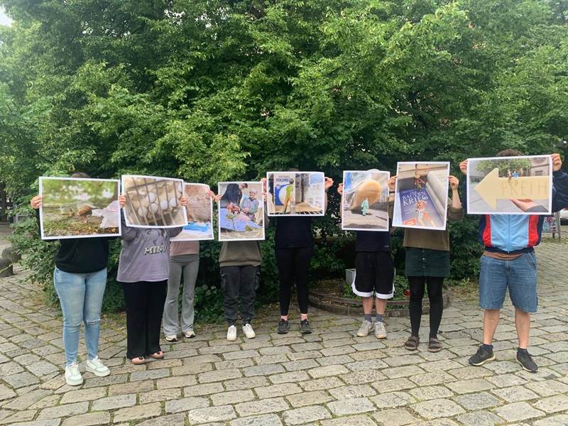 Kleine Kunst – große Kämpfe Die Auszubildenden der Euro Akademie Würzburg stehen nebeneinander und halten ihre selbst gestalteten Bilder hoch und vor das eigene Gesicht.
