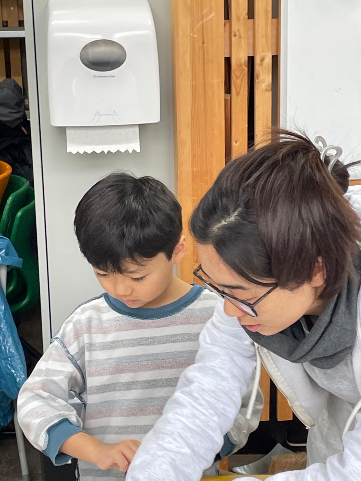 Erwachsene Person unterstützt ein Grundschulkind konzentriert bei einer Druckarbeit; Nahaufnahme am Werktisch.