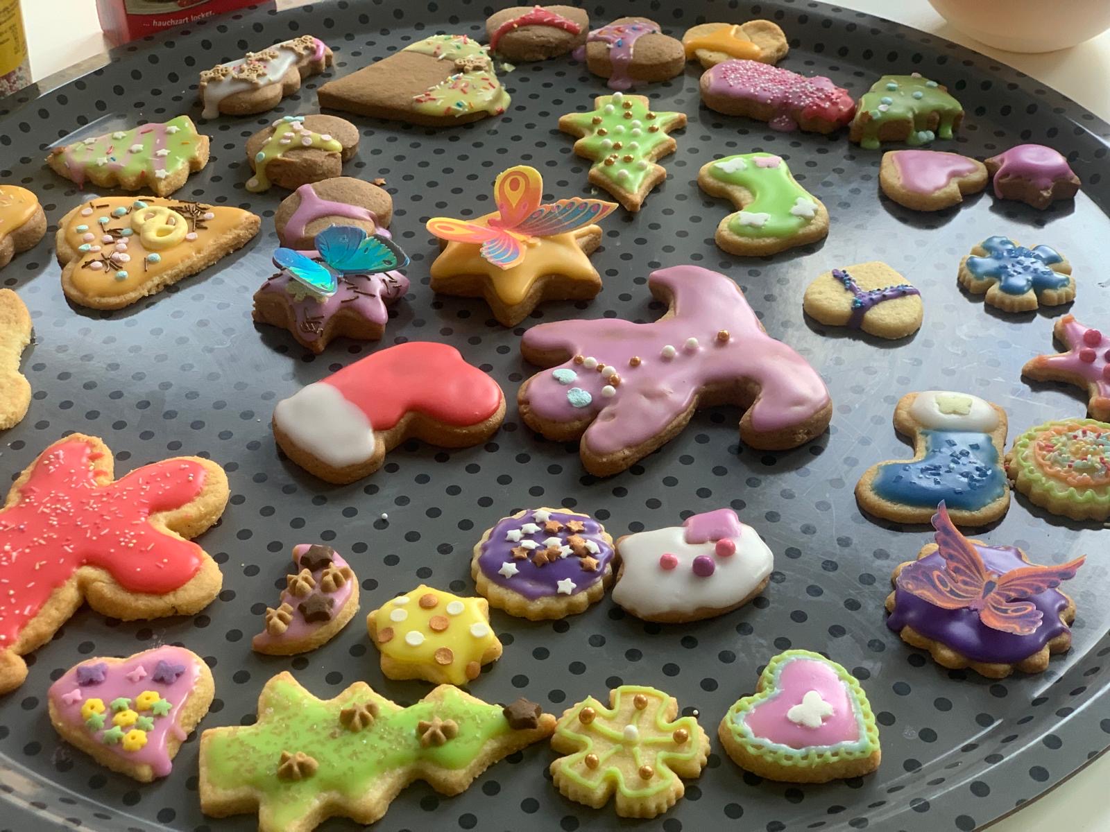 Nahaufnahme eines Tabletts voller bunter, kreativ glasierter Weihnachtsplätzchen in verschiedenen Formen wie Sterne, Herzen und Stiefel.