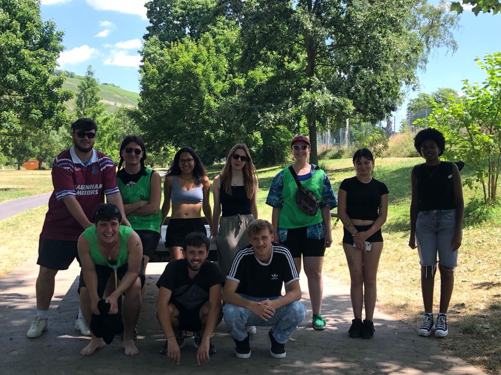 Eine Gruppe von Personen posiert für ein Foto in einem Park. Einige tragen grüne Westen und lächeln in die Kamera.