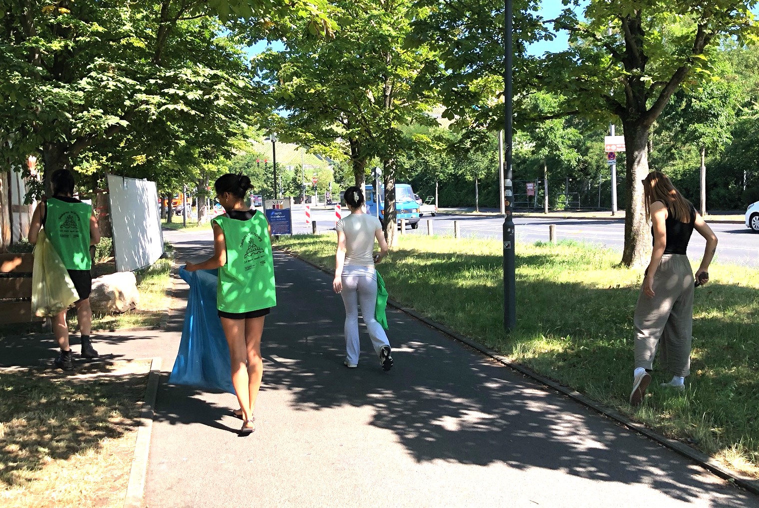 Müllsammelaktion an den Mainwiesen – Gemeinsam für eine saubere Umwelt! Eine Gruppe von Personen in grünen Westen sammelt Müll auf einem Gehweg. Einige Personen tragen blaue Müllsäcke.