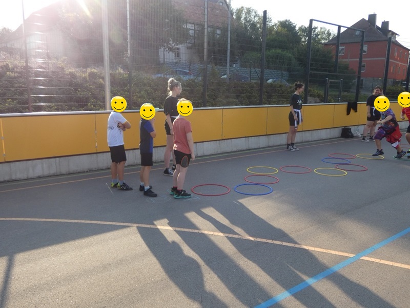 Kinder laufen hintereinander über den Parcours auf dem Outdoor-Sportplatz, bei dem sie in die ausgelegten Hula Hoop Reifen springen müssen. 