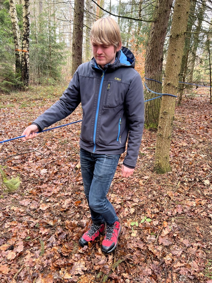 Ein Schüler hält sich an einem blauen Seil fest und läuft mit geschlossenen Augen von einem Baum zum nächsten.