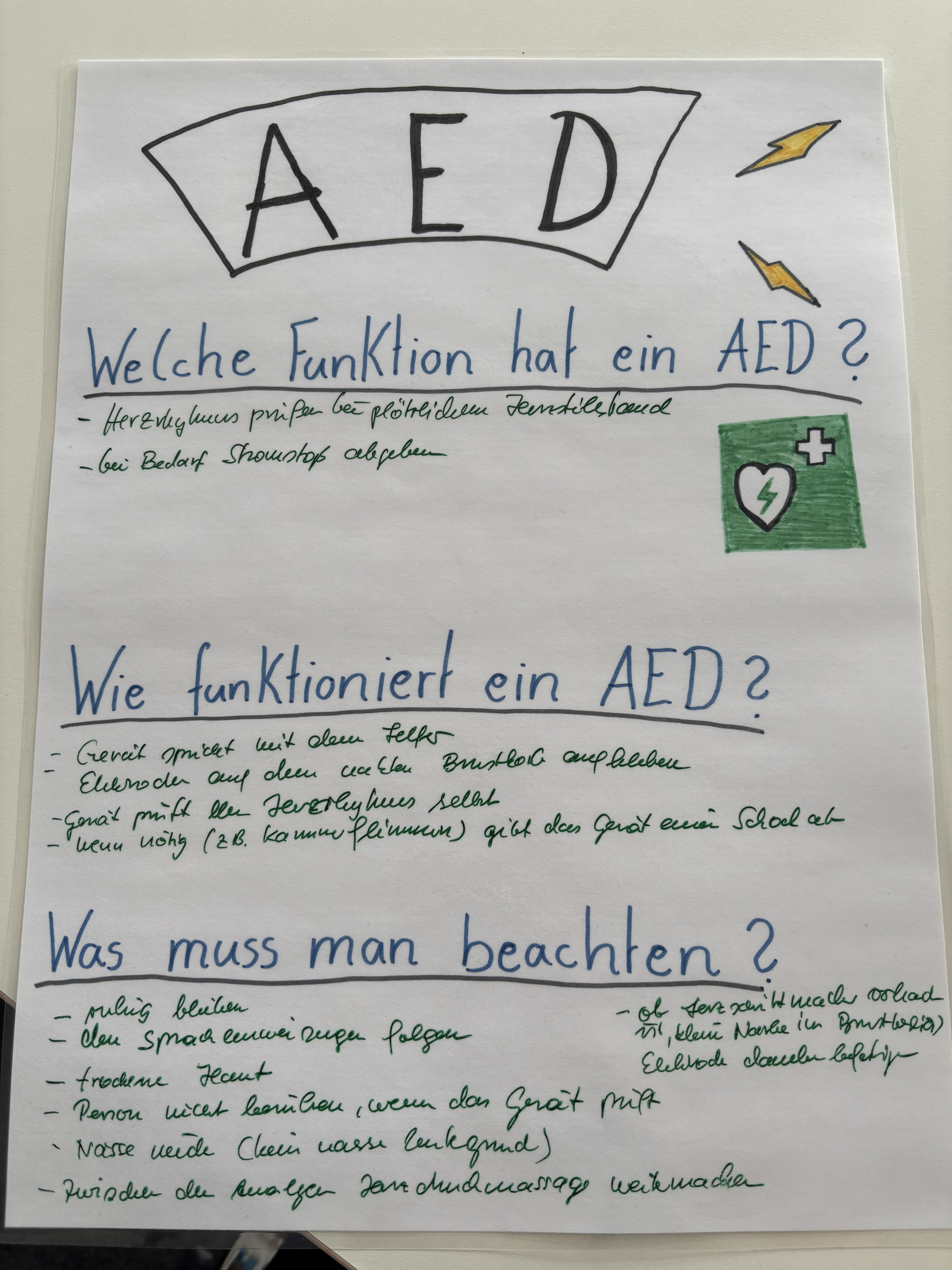 Handgestaltetes Lernplakat über die Funktion und Anwendung eines automatisierten externen Defibrillators, kurz AED, sowie wichtige Hinweise zur Nutzung.