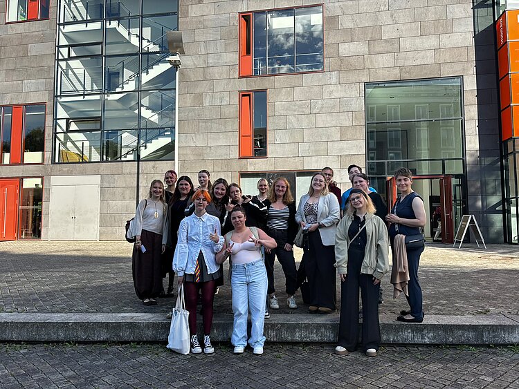 Gruppenbild von Schülerinnen und Schülern vor einem Steingebäude mit orangefarbenen Fensterläden und verglastem Treppenhaus.