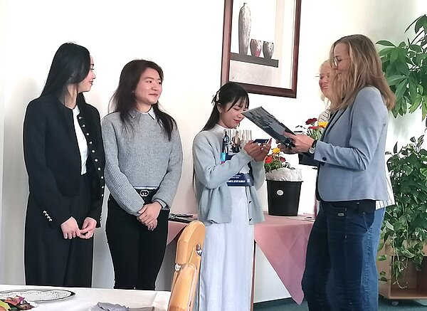 Mehrere Absolventinnen der Pflegefachkraft-Ausbildung stehen während der feierlichen Zeugnisübergabe an der Euro Akademie Bitterfeld-Wolfen nebeneinander. Die Schulleiterin überreicht einer Absolventin freudig ihr Abschlusszeugnis.