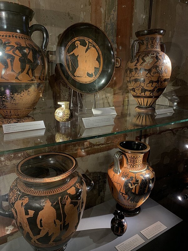 Eintauchen in die römische Kultur In einer Glasvitrine stehen unterschiedliche Keramikvasen und -Teller in den Farben schwarz und beige.