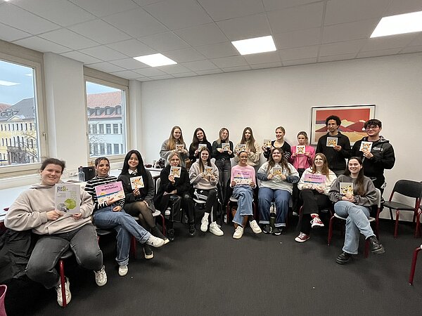 Wo die Katze nicht gestreichelt werden will Für ein Gruppenfoto haben sich die Schüler*innen in einer Ecke des Klassenzimmers gesammelt. Sie sitzen und stehen teilweise. Jede*r Schüler*in hält ein Buch bzw. eine Broschüre des Projekts ReSi in die Kamera.