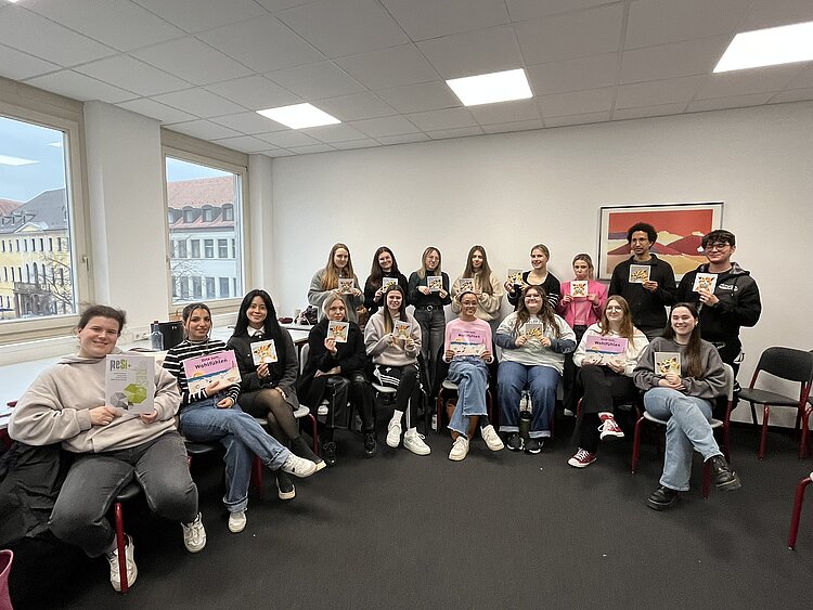 Wo die Katze nicht gestreichelt werden will Für ein Gruppenfoto haben sich die Schüler*innen in einer Ecke des Klassenzimmers gesammelt. Sie sitzen und stehen teilweise. Jede*r Schüler*in hält ein Buch bzw. eine Broschüre des Projekts ReSi in die Kamera.