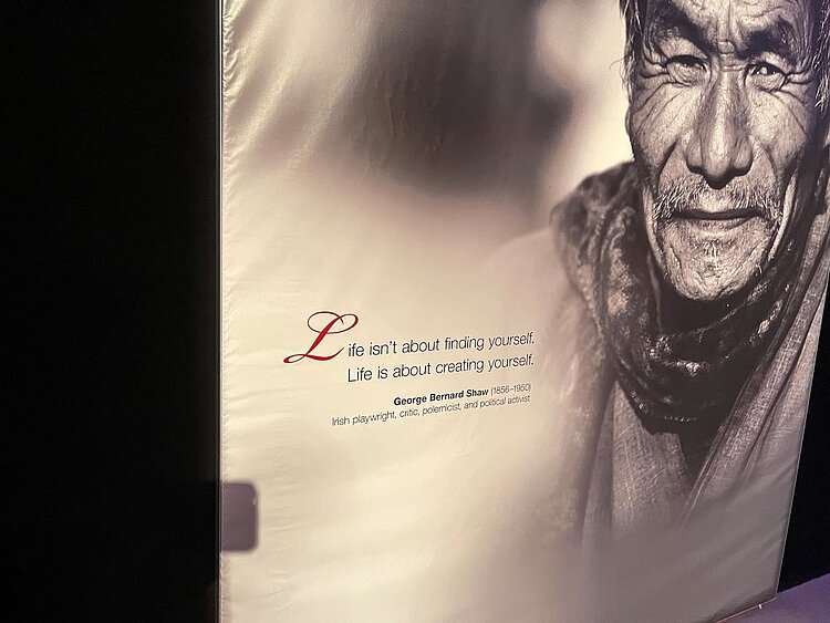 Echte Körper - echt faszinierend Ein schwarz-weißes Wandbild mit dem Porträt eines älteren Mannes. Daneben steht ein Zitat von George Bernard Shaw: „Life isn’t about finding yourself. Life is about creating yourself.“
