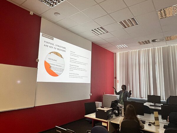 Eine Präsentation zum Thema Lebenslauf und Bewerbung wird in einem Computerraum vor einer Gruppe von Teilnehmenden gezeigt.