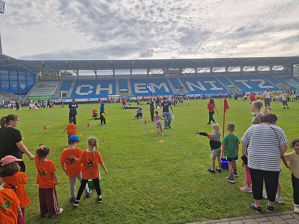 Zahlreiche Kindergruppen und Betreuungspersonen verteilen sich auf dem Rasen des Chemnitzer Stadions und nehmen an verschiedenen Bewegungs- und Spielstationen teil.