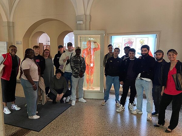 Die rund 15 weiblichen und männlichen Auszubildenden zu Pflegefachkräften an der Euro Akademie Jena  stehen im Ausstellungssaal, hinter ihnen ein Exponat eines menschlichen Körpers, des Universitätsklinikums Jena und posieren, gemeinsam mit ihrer Lehrerin, lächelnd für ein Foto.