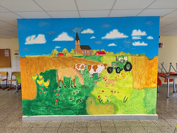 Erzieher*innen begleiten die Kreativtage an der Förderschule für geistige Entwicklung in Skäßchen Eine große, farbenfrohe Wandmalerei mit einer ländlichen Szene. Zu sehen sind eine Kirche, Felder, Tiere wie Kühe, Hühner und ein Pferd sowie ein grüner Traktor. Der Himmel ist blau mit weißen Wolken. Das Bild befindet sich in einem Schulgebäude mit Stühlen und Tischen im Hintergrund.