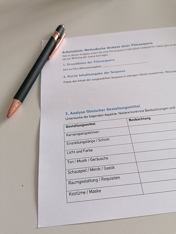Arbeitsblatt „Methodische Analyse einer Filmsequenz“ mit Stift auf dem Tisch.