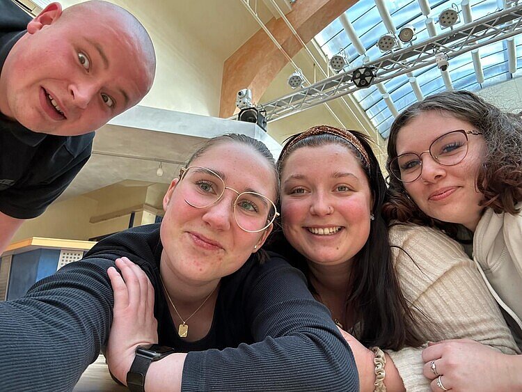 Fit für die Prüfung mit Bewegung Ein Selfie aus nächster Nähe: Die drei Schülerinnen und der eine Schüler schauen direkt in die Handykamera. Man kann im Hintergrund die Glasdecke des Tanzsaals sehen, unter der Scheinwerfer befestigt sind.