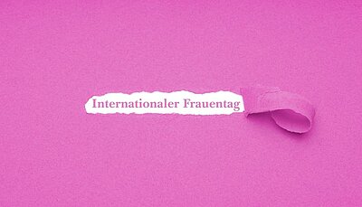 Ein pinkes Blatt Papier, aus dem ein Streifen gerissen ist: dort steht "Internationaler Frauentag".