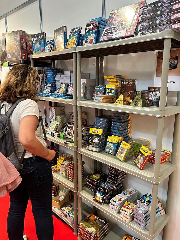 Ein besonderer Tag in Leipzig - Exkursion zur „Hobbymesse“ Eine Schülerin, die nur von hinten zu sehen ist, betrachtet mehrere große Regale voller unterschiedlicher Spiele.