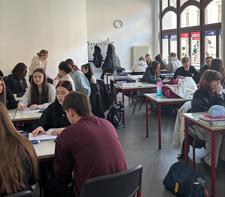 Schülerinnen und Schüler sitzen in Gruppen in einem großen, hellen Klasseraum für eine gemeinsame Unterrichtsstunde.