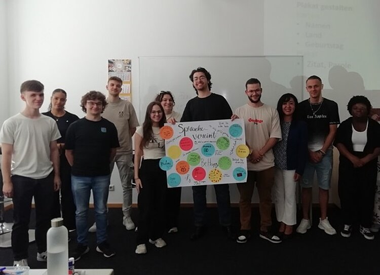 Die Auszubildenden posieren für ein Klassenfoto und halten ihre selbst gestaltete Collage hoch, auf dem ihre Namen und Geburtstage stehen.