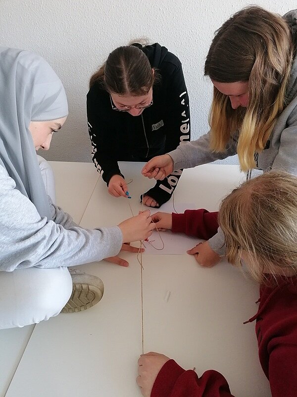 Teamwork Vier Schülerinnen beugen sich konzentriert über ihre Gruppenaufgabe, die auf einem Tisch aufgebaut ist und an der sie gemeinsam arbeiten.