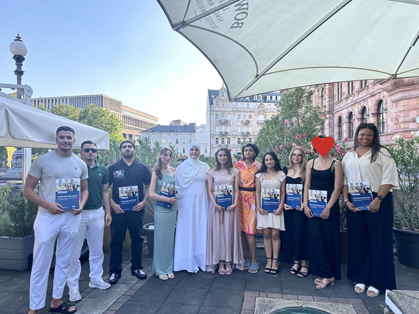 Gruppenfoto von Absolvent*innen und Begleitpersonen im Außenbereich, mehrere Personen halten Broschüren in den Händen.
