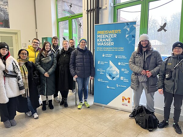 Der nächste Schritt zur Karriere: Career Week Eine Gruppe von Schüler*innen in dicker, winterlicher Kleidung steht im Vorraum eines Wasswerks, direkt neben einem Rollup mit dem Titel "Preiswert: Meenzer Kranewasser".