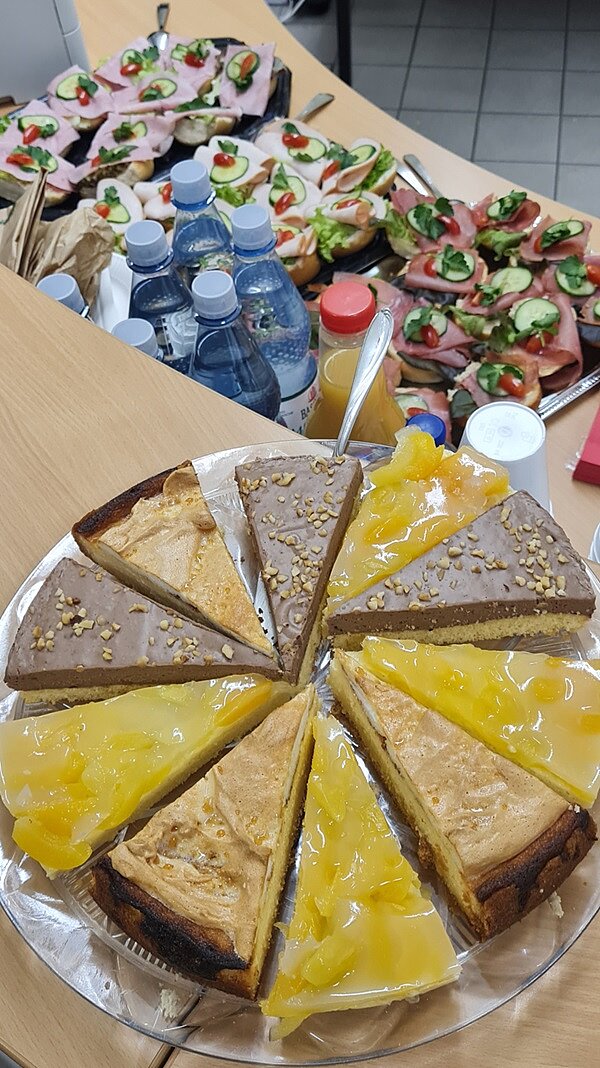 Buffet mit belegten Brötchen, Kuchen, Wasser und Fruchtsaft.